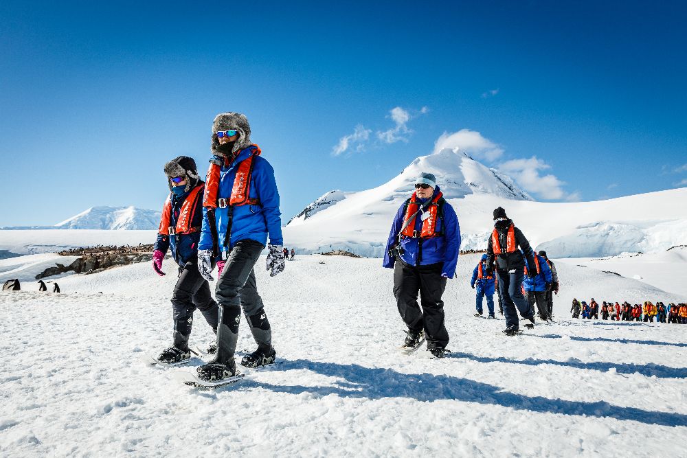 Group of people in colorful jackets walking on snowy landscape with mountains
